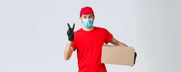 Packages and parcels delivery covid19 quarantine delivery transfer orders Friendly courier in red uniform face mask and gloves deliver order to client holding box show peace sign