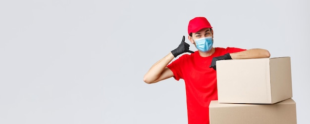 Packages and parcels delivery covid19 quarantine and transfer orders Friendly courier in red uniform face mask and gloves asking customer give call show phone sign stand near boxes