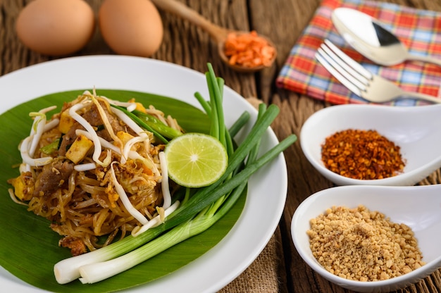 Pad Thai in a white plate with lemon, eggs and seasoning on a wooden table.