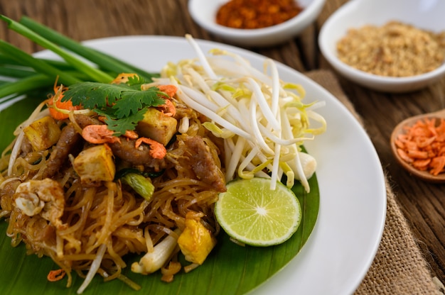 Pad Thai in a white plate with lemon, eggs and seasoning on a wooden table.