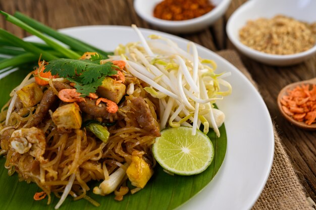 Pad Thai in a white plate with lemon, eggs and seasoning on a wooden table.