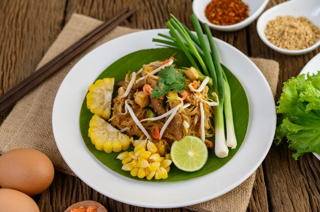 Pad Thai in a white plate with lemon, eggs and seasoning on a wooden table.