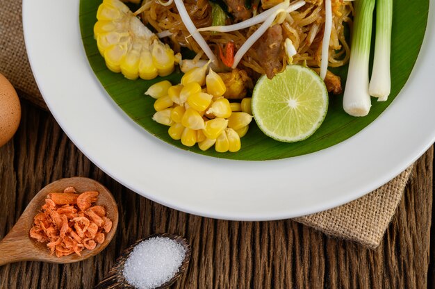 Pad Thai in a white plate with lemon, eggs and seasoning on a wooden table.