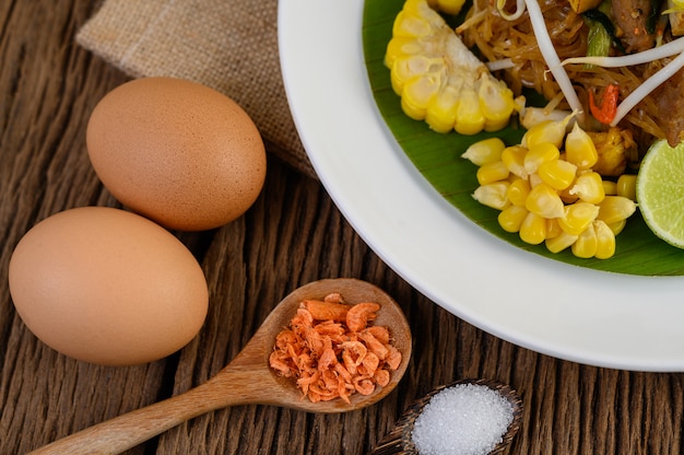 Pad Thai in a white plate with lemon, eggs and seasoning on a wooden table.