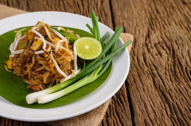 Pad Thai in a white plate with lemon on a wooden table