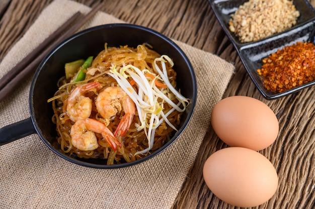 Padthai shrimp in a black bowl with eggs and Seasoning on wooden table.