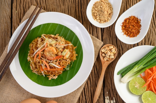 Gamberetto di padthai in una ciotola nera con le uova, la cipolla di inverno e il condimento sulla tavola di legno.