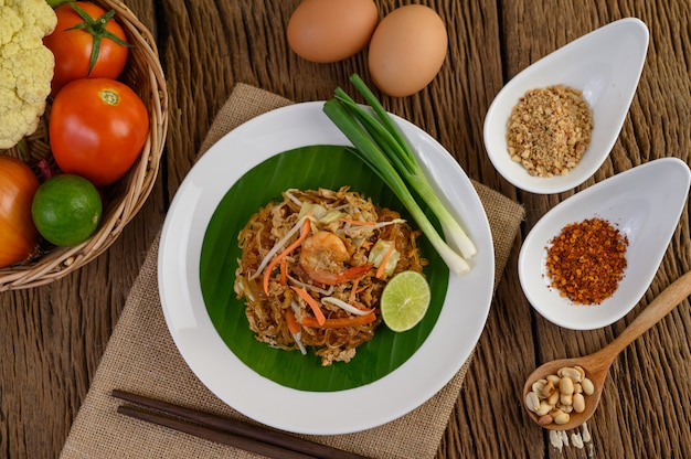 Free photo padthai shrimp in a black bowl with eggs, spring onion, and seasoning on wooden table.