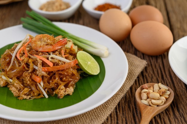 Padthai shrimp in a white dish with lime and eggs on wooden table.