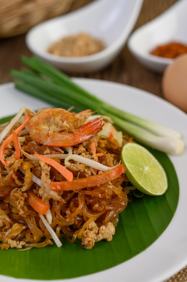 Free Photo padthai shrimp in a white dish with lime and eggs on wooden table.