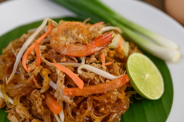 Padthai shrimp in a white dish with lime and eggs on wooden table