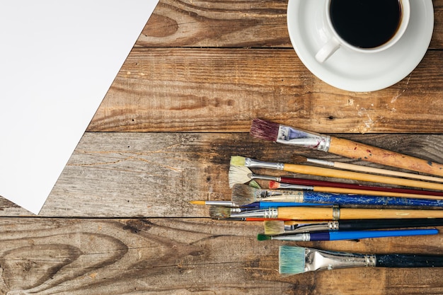 Free photo paint brushes and a cup of coffee on a wooden background flat lay