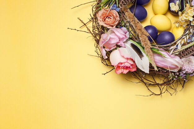 Окрашенные пасхальные яйца в гнезде на желтом фоне стола. Вид сверху пасхального украшения. Счастливой пасхи концепции. Модные цвета