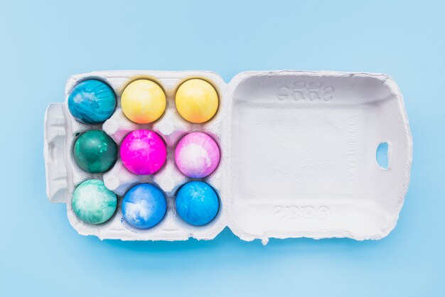 Painted eggs in carton box on blue background