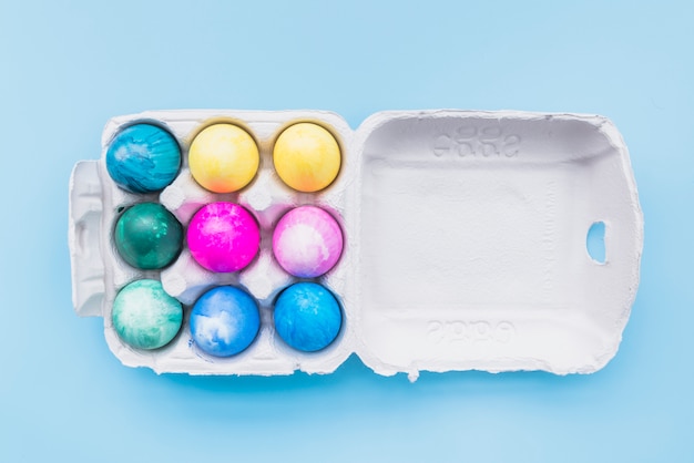 Крашеные яйца в картонной коробке на синем фоне