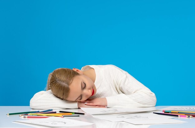 Painter cute young blonde girl paintaing and sleeping on the table in the pile of pencils