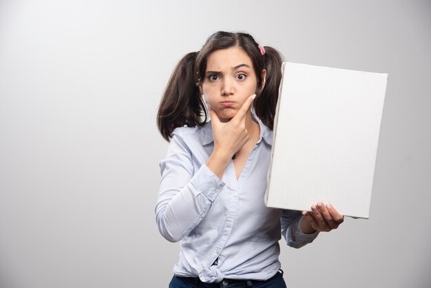 Painter with ponytail holding empty canvas on gray wall. 