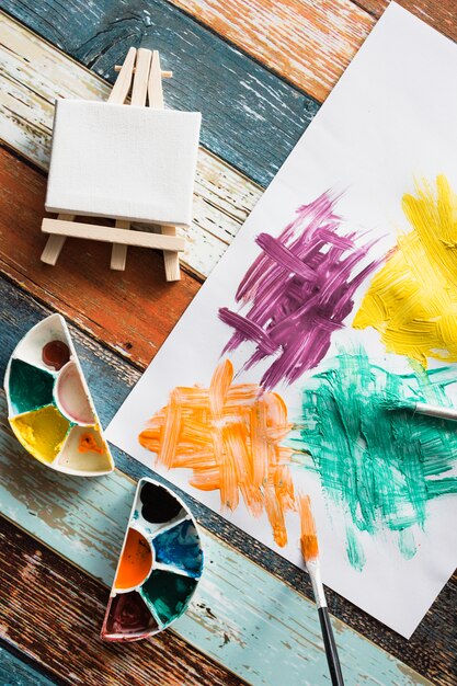 Painting equipment and messy painted paper on wooden backdrop