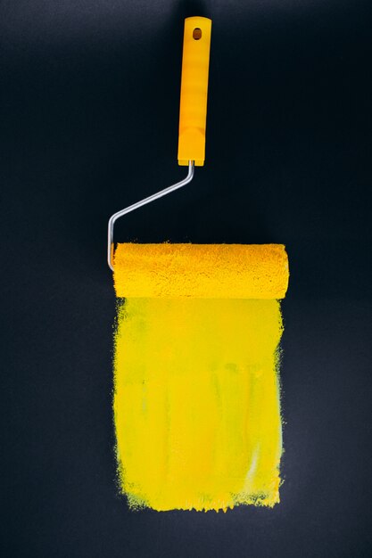 黄色の塗料で黒の背景に分離された修理用Paintroller