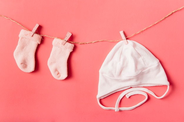 Pair of baby's sock and cap hanging with clothespin on string against colored backdrop