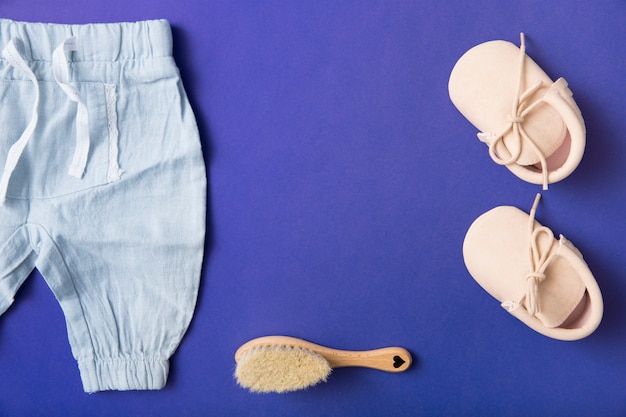Pair of baby shoes; brush and baby's pant on bright blue background