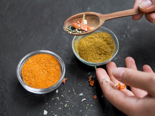 Pair of bowls full of spices with hand holding spoon