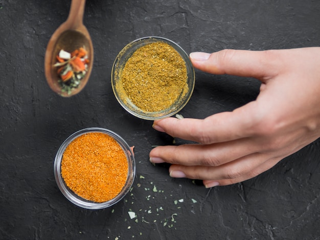 Pair of bowls full of spices with hand and spoon