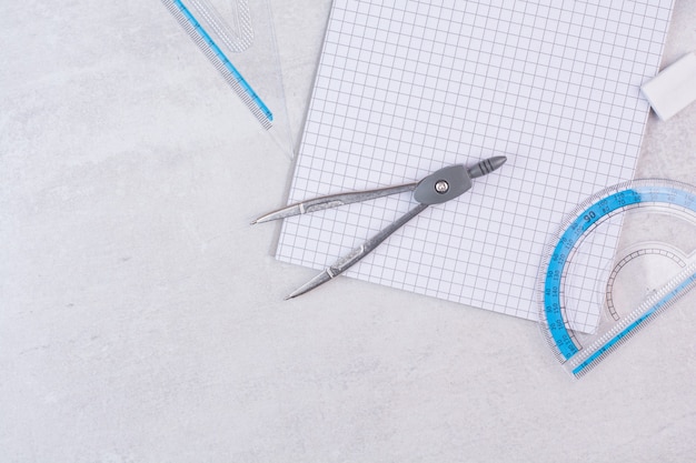 Pair of geometry compasses and paper on white surface