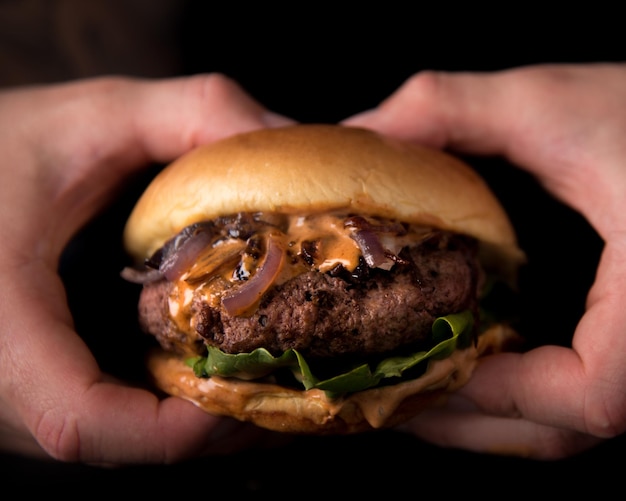 Un paio di mani che tengono un hamburger fresco e succoso con lattuga, cipolle e formaggio su sfondo nero