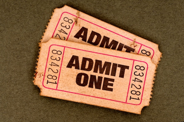 Free photo pair of old torn admit one movie tickets on a brown background.