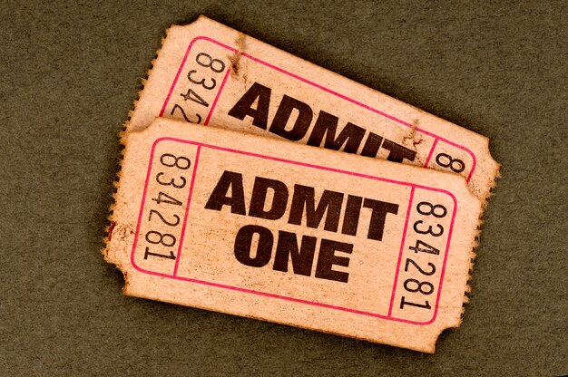 Pair of old torn admit one movie tickets on a brown background.