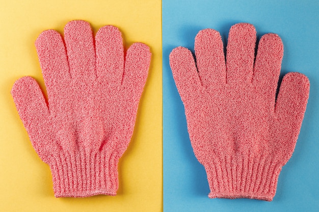 A pair of pink massage gloves for shower on blue and yellow background Premium Photo