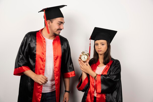 Pair of students in gown with clock standing on white.