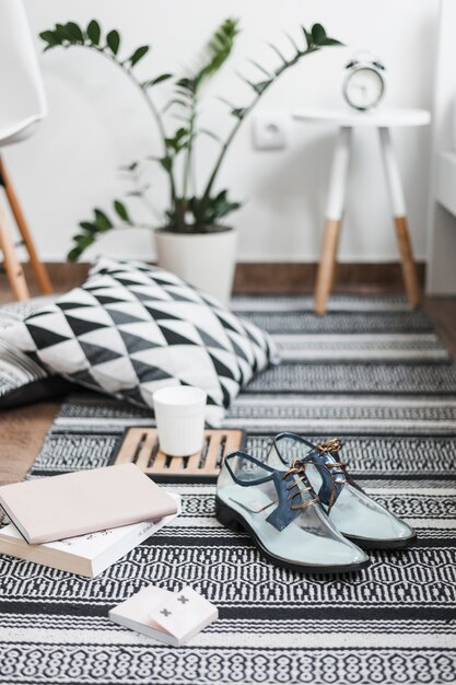 Pair of trendy transparent shoes with books, adhesive note and coffee mug on rug