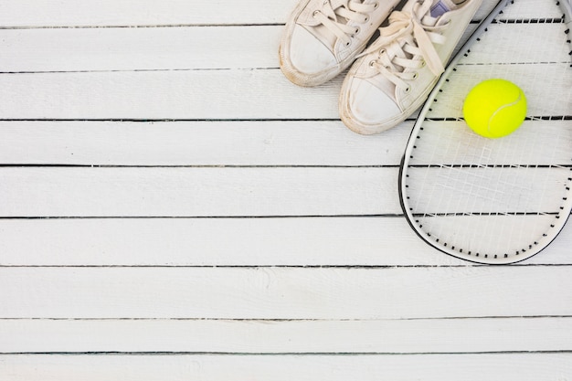 Pair of white sport shoes and racket with tennis ball on wooden table