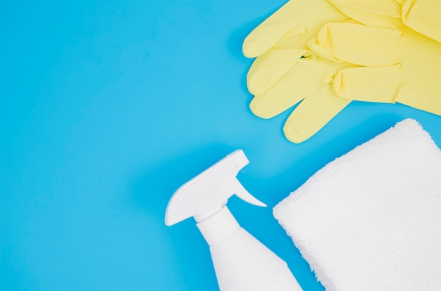 Pair of yellow gloves with white bottle and sponge on blue backdrop