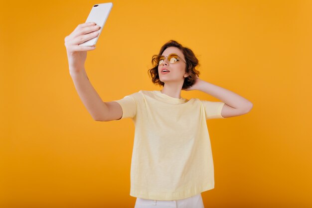 Pale girl with taking picture of herself in yellow room