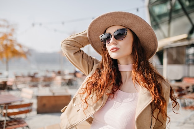 Pale woman with wavy dark hair looking up and touching her hat