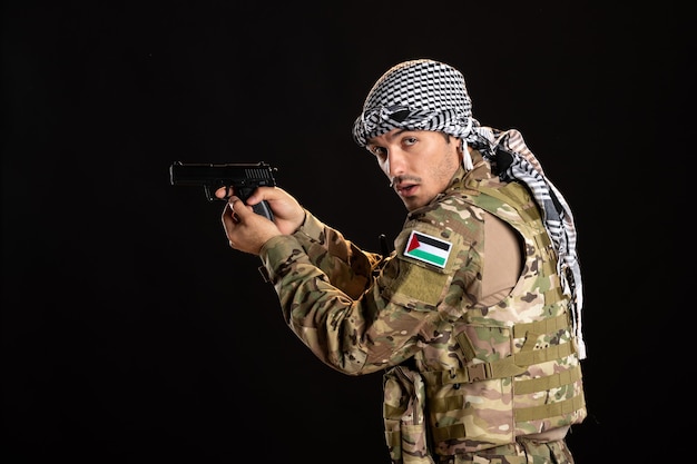 Foto gratuita soldato palestinese che punta la pistola contro il muro nero