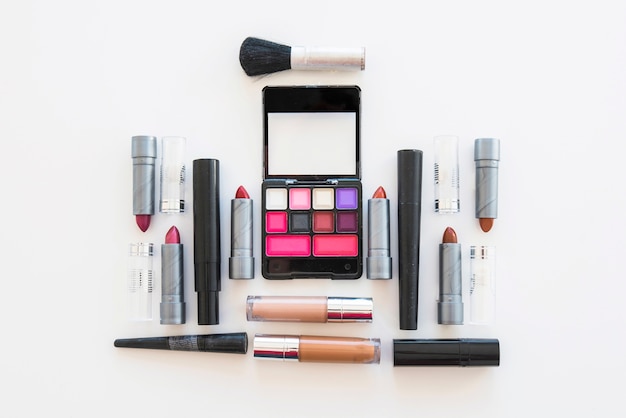 Free photo palette of cosmetic eye shadow; different shades of lipstick; and brush on white backdrop