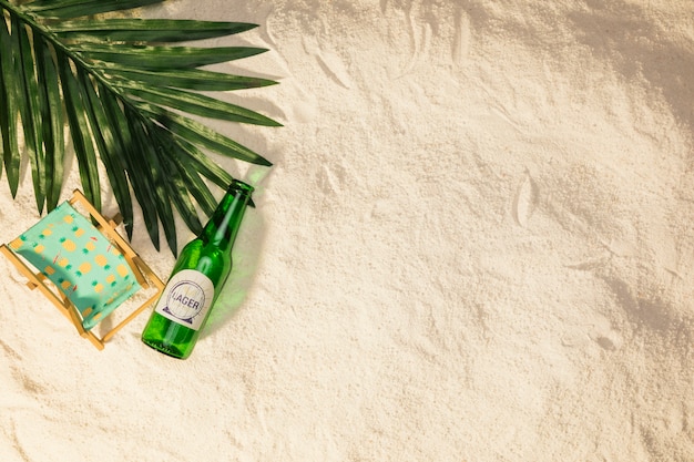 Free photo palm tree leaf bottle of drink and small deckchair on sand