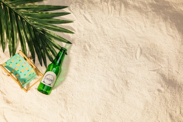 Palm tree leaf bottle of drink and small deckchair on sand