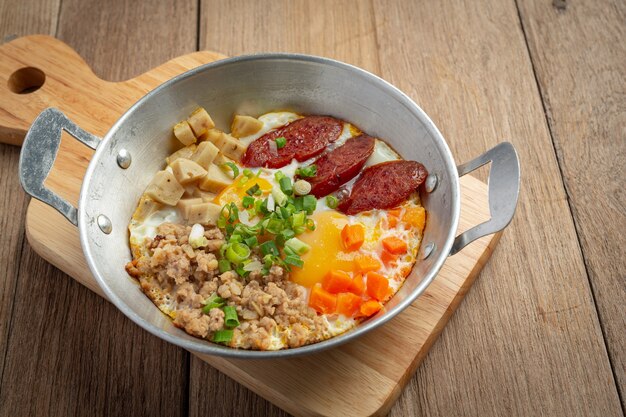 Яйца на сковороде, посыпанные китайской колбасой, нарезанный кубиками бекон, завтрак.