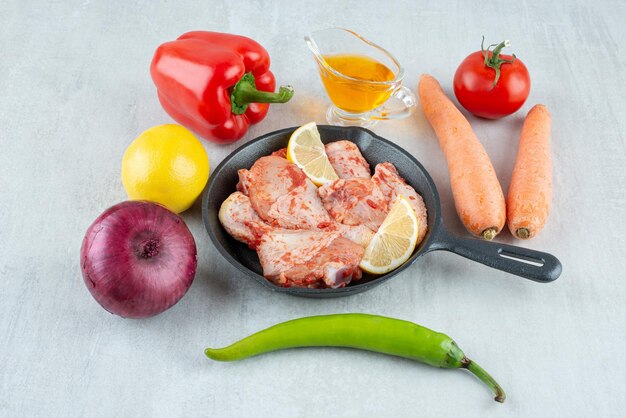 Pan of seasoned chicken, oil and vegetables on stone surface.