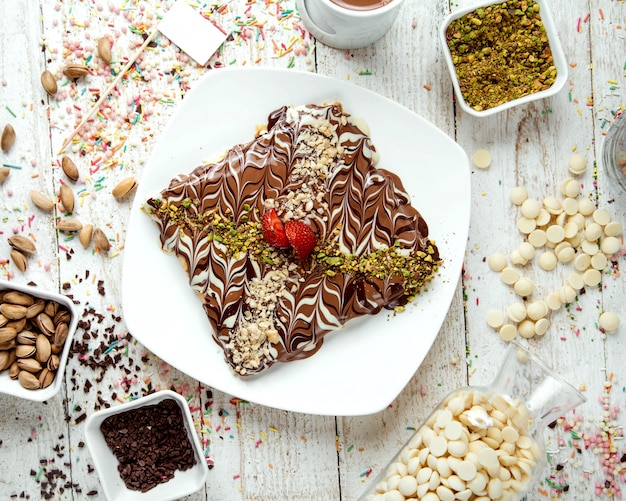 초콜릿 시럽으로 덮인 팬케이크와 강판 피스타치오 평면도로 뿌린다.