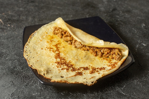 pancake with meat inside black plate on dark