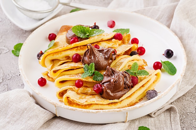 Pancakes with berries and chocolate decorated with mint leaf. Tasty breakfast.