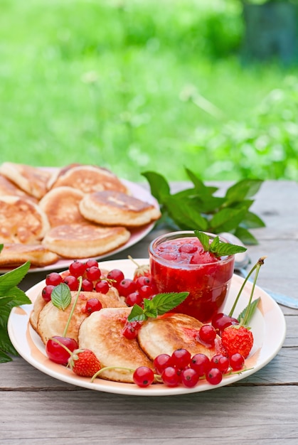 Pancakes with berries on a wooden table in a summer garden