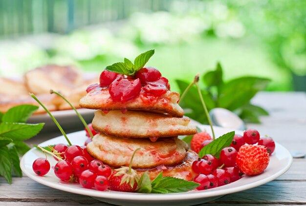 Pancakes with berries on a wooden table in a summer garden