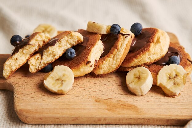 Pancakes with chocolate sauce, berries, and banana on a wooden plate behind on white